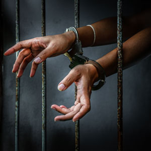 Handcuffed hands reaching through the bars of a jail cell, symbolizing arrest and detention.